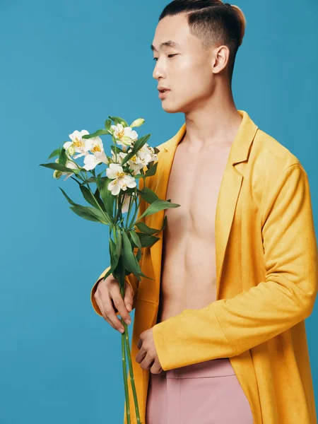 Un joven de aspecto asiático con un ramo de flores se ve a un lado sobre un fondo azul —  Fotos de Stock
