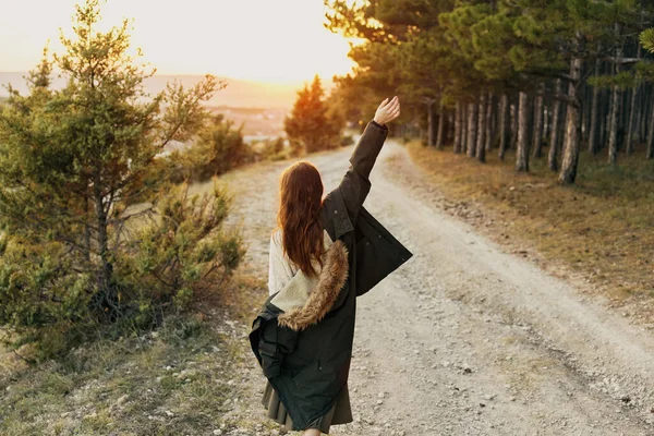 A woman with a raised hand warm jacket on the nature road near the forest