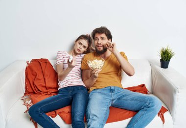 Kanepede patlamış mısırlı bir adam ve kadın televizyon seyrediyor.