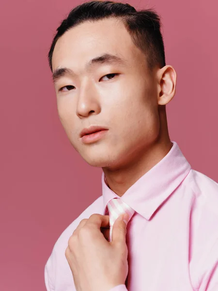 Asian man in pink shirt straightens his tie cropped view