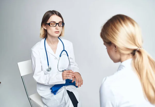 Dokter zit op een stoel en een vrouw patiënt binnen op een lichte achtergrond — Stockfoto
