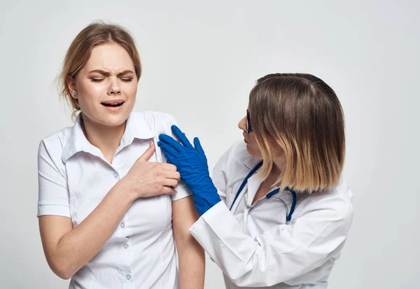 Une infirmière en gants bleus examine un patient en T-shirt blanc sur un fond clair — Photo