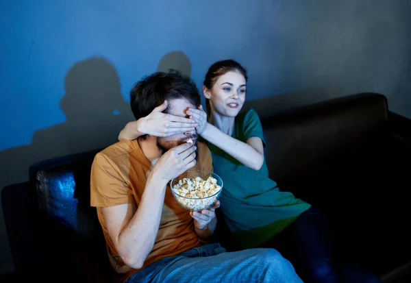 Energetisches Frauenmodel auf einem Ledersofa und ein Mann Popcorn im Abendteller — Stockfoto