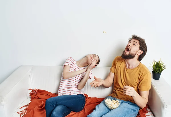 Fun man and energetic woman watching TV on the couch popcorn in a plate family communication