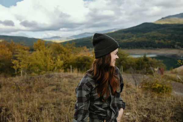 Mujer sonriente en un sombrero en un prado en las montañas mira a un lado y se ríe — Foto de Stock