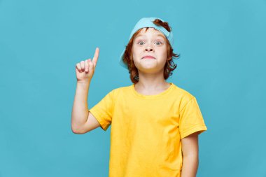 Şaşırmış kızıl çocuk sarı tişörtü işaret ediyor mavi başlık Boşluğu kopyala