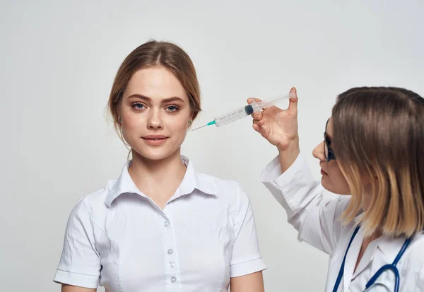 Kvinnlig läkare visar patienten en spruta och en medicinsk klänning ett stetoskop — Stockfoto