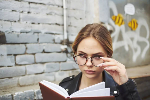 Vrouw in een zwarte jas met een notitieboekje in haar handen in de buurt van een bakstenen gebouw bijgesneden uitzicht — Stockfoto