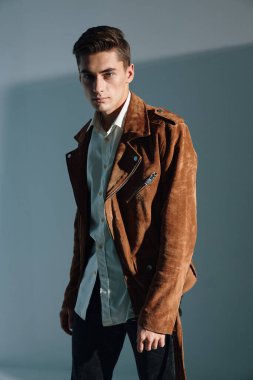 Gri arka planda kahverengi ceketli, kendine güvenen bir adam.