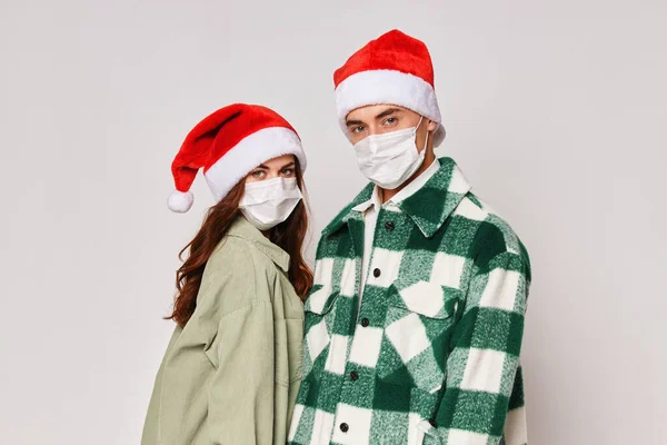 Homme et femme en masques médicaux Chapeaux de Noël vacances fond gris — Photo