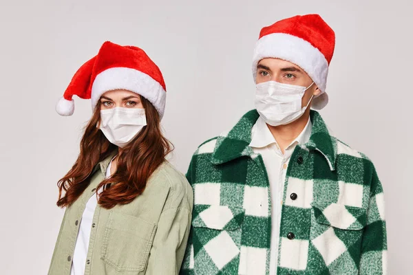 Молода пара в медичних масках на обличчі Різдвяні капелюхи стоять поруч зі святом Різдво — стокове фото