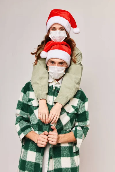 Чоловік і жінка в різдвяних капелюхах приймають святкові медичні маски — стокове фото