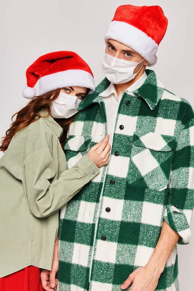 Молода пара в різдвяних капелюхах медичні маски на обличчі обіймає свято — стокове фото