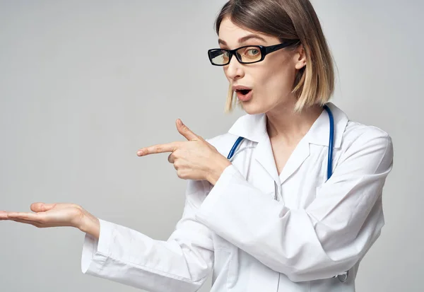 Enfermera con un vestido médico haciendo gestos con las manos sobre un fondo claro —  Fotos de Stock