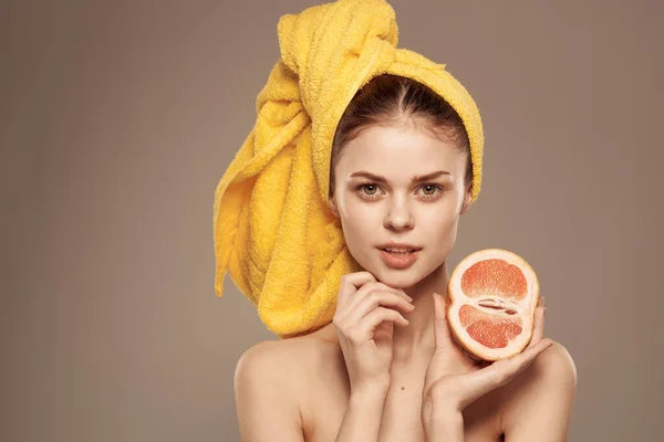 Donna con spalle nude asciugamano giallo sulla testa pompelmo nelle mani la cura della pelle pulita — Foto Stock