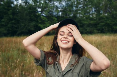 Çayırda tişörtlü bir kadın yüzüne dokunuyor. 