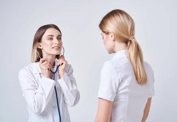 Läkare i en medicinsk klänning på en ljus bakgrund och en blond kvinna patient — Stockfoto