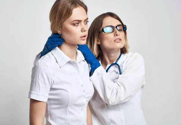 Un'infermiera in guanti blu esamina un paziente con una maglietta bianca su uno sfondo chiaro — Foto Stock
