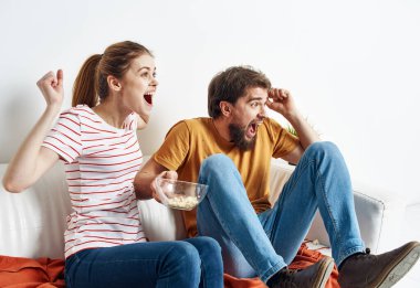 İlgili kadın ve sakallı adam kanepede oturur bir tabakta patlamış mısır ve saksıda çiçek