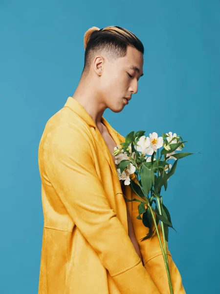 Ο τύπος με το κίτρινο παλτό. Ασιατική εμφάνιση. Μπουκέτο με λευκά λουλούδια και μπλε φόντο — Φωτογραφία Αρχείου
