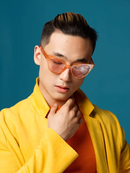 Un homme aux lunettes orange et un T-shirt jaune sur fond bleu se touche le cou avec sa main — Photo