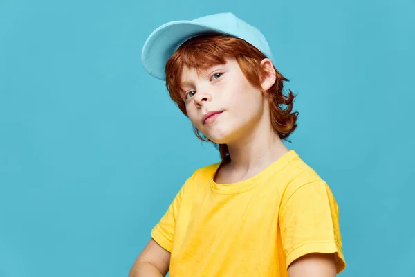 Rudy chłopiec pochylił głowę do jednej strony niebieski czapka żółty t-shirt studio — Zdjęcie stockowe