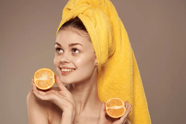 Mulher bonita desnudado ombros laranjas nas mãos de uma toalha amarela em sua cabeça — Fotografia de Stock