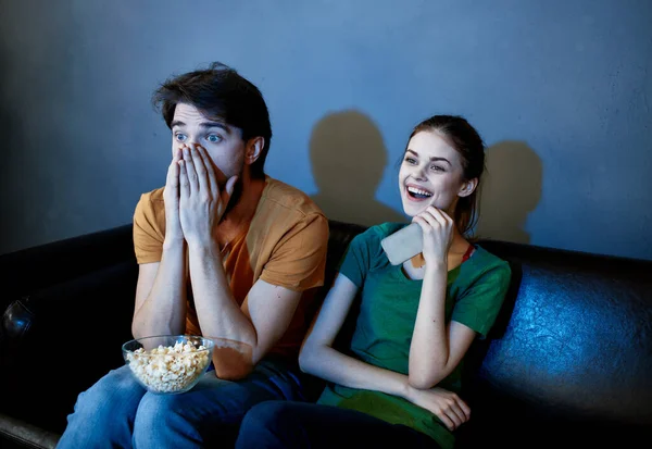 Scared man and happy woman watching TV in the evening on the couch — Stock Photo, Image