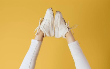 Kadın ayakları beyaz spor ayakkabılar moda sarı arka plan