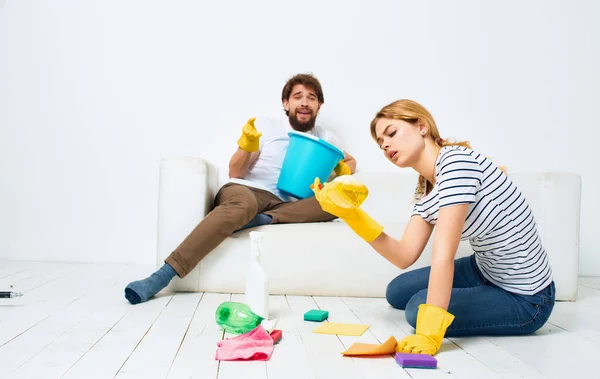 Adam kanepede yatıyor ve kadın yerdeki deterjanı temizliyor. — Stok fotoğraf