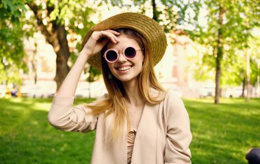 Şapkalı ve güneş gözlüklü güzel bir kadın açık havada parkta yürür.