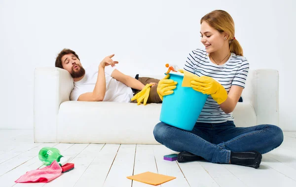 The man lies on the couch and the woman is cleaning the detergent on the floor — Stock Photo, Image
