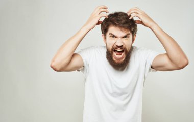 Kafasını tutan sakallı adam elleri beyaz tişörtle hareket eder.