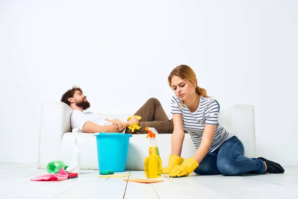 Чоловік лежить на дивані жінка миє підлогу, надаючи послуги внутрішньої домашньої роботи — стокове фото