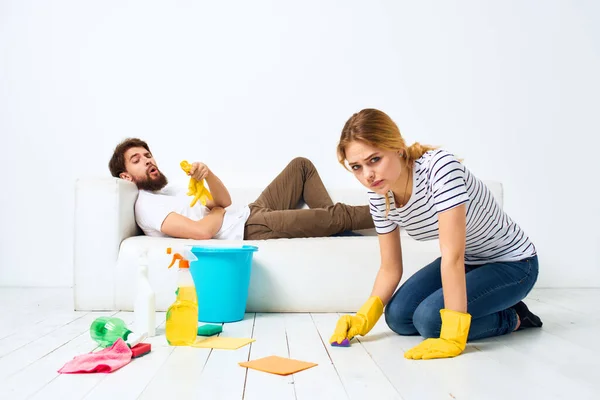 The man lies on the sofa woman washes the floors providing services interior housework — Stock Photo, Image