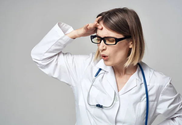 Médico en un vestido médico con un estetoscopio alrededor de su cuello desconcertado mirada fondo gris —  Fotos de Stock