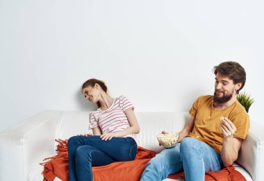 Bir kadın kanepede dinleniyor ve bir adam elinde patlamış mısır çiçeğiyle kırmızı ekose bir tencerede