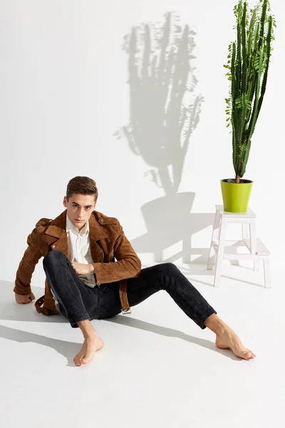Een jonge man in een pak zit blootsvoets op de vloer naast een bloem in een pot — Stockfoto