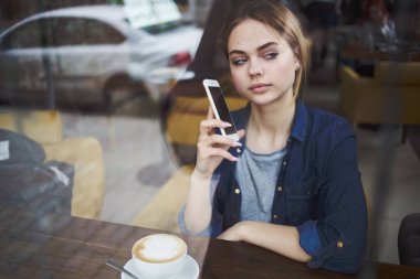 Kadın, sabah yaşam tarzında bir fincan kahveyle masadaki bir kafeden iletişim kuruyor.