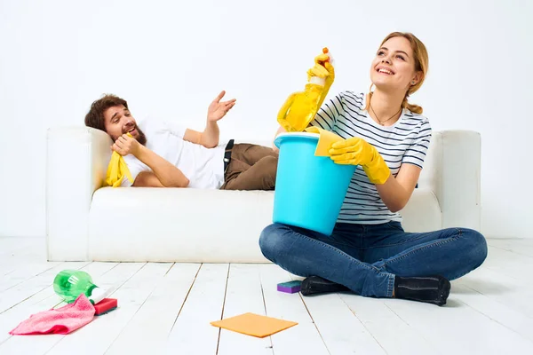 woman with a bucket in rubber gloves at home husband lies on the couch cleaning