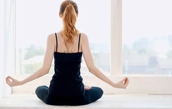 Mujer haciendo yoga en el interior cerca de la ventana y haciendo gestos con las manos hacia atrás — Foto de Stock