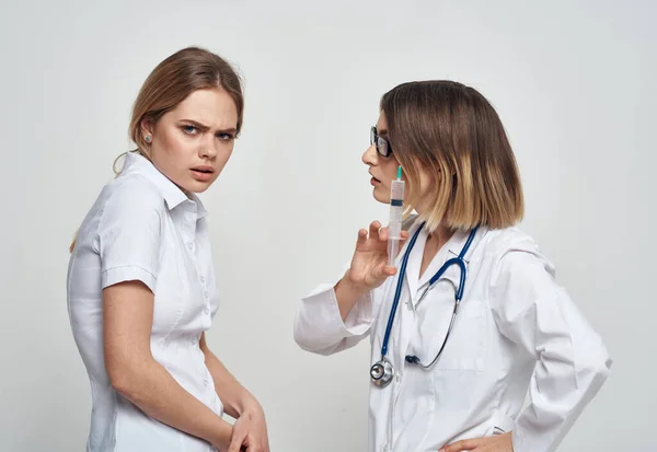 Возмущённая пациентка общается с медсестрой в медицинском платье и со шприцем в руке. — стоковое фото