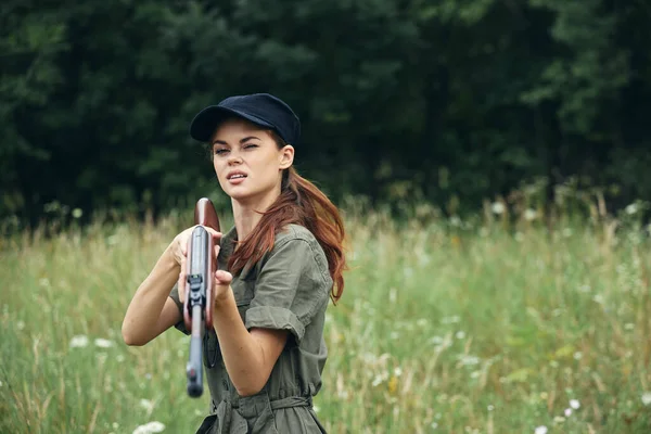 Mujer en la naturaleza mujer sosteniendo un arma Mirada hacia adelante la caza gorra negra — Foto de Stock