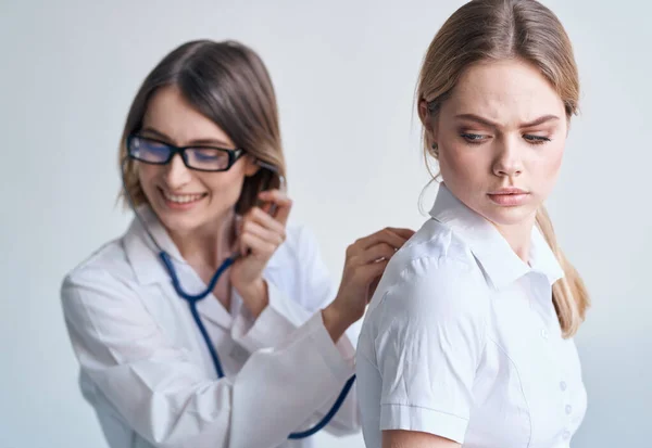 La paciente le dio la espalda al médico con una bata médica con un estetoscopio — Foto de Stock