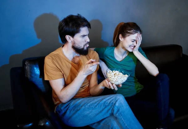 Energetisches Frauenmodel auf einem Ledersofa und ein Mann Popcorn im Abendteller — Stockfoto