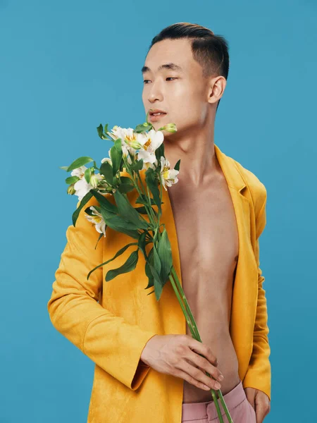 Ένας ημίγυμνος άντρας με ένα μπουκέτο λευκά λουλούδια που κοιτάει στο πλάι με μπλε φόντο και ένα κίτρινο παλτό. — Φωτογραφία Αρχείου