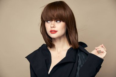 Güzel, koyu renk ceketli, parlak makyajlı bir kadın bej arka planda seviniyor. 