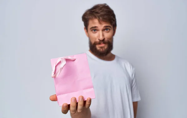 Homme barbu en t-shirt blanc tenant sac cadeau rose dans les mains fond isolé — Photo