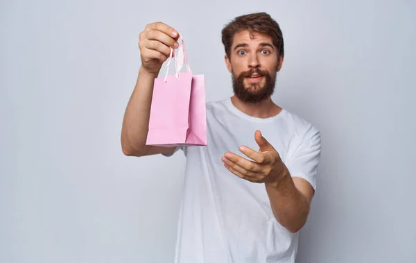 Homem barbudo em t-shirt branca segurando saco de presente rosa em mãos isolado fundo — Fotografia de Stock