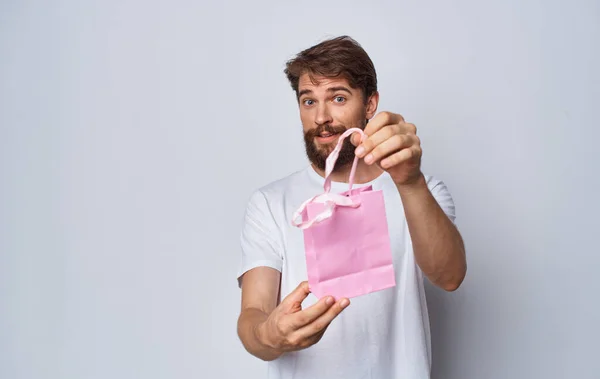 Homem barbudo em t-shirt branca segurando saco de presente rosa em mãos isolado fundo — Fotografia de Stock